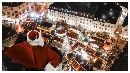 Ein Weihnachtsmann von Hinten fliegt über den abendlichen Saarbrücker Weihnachtsmarkt